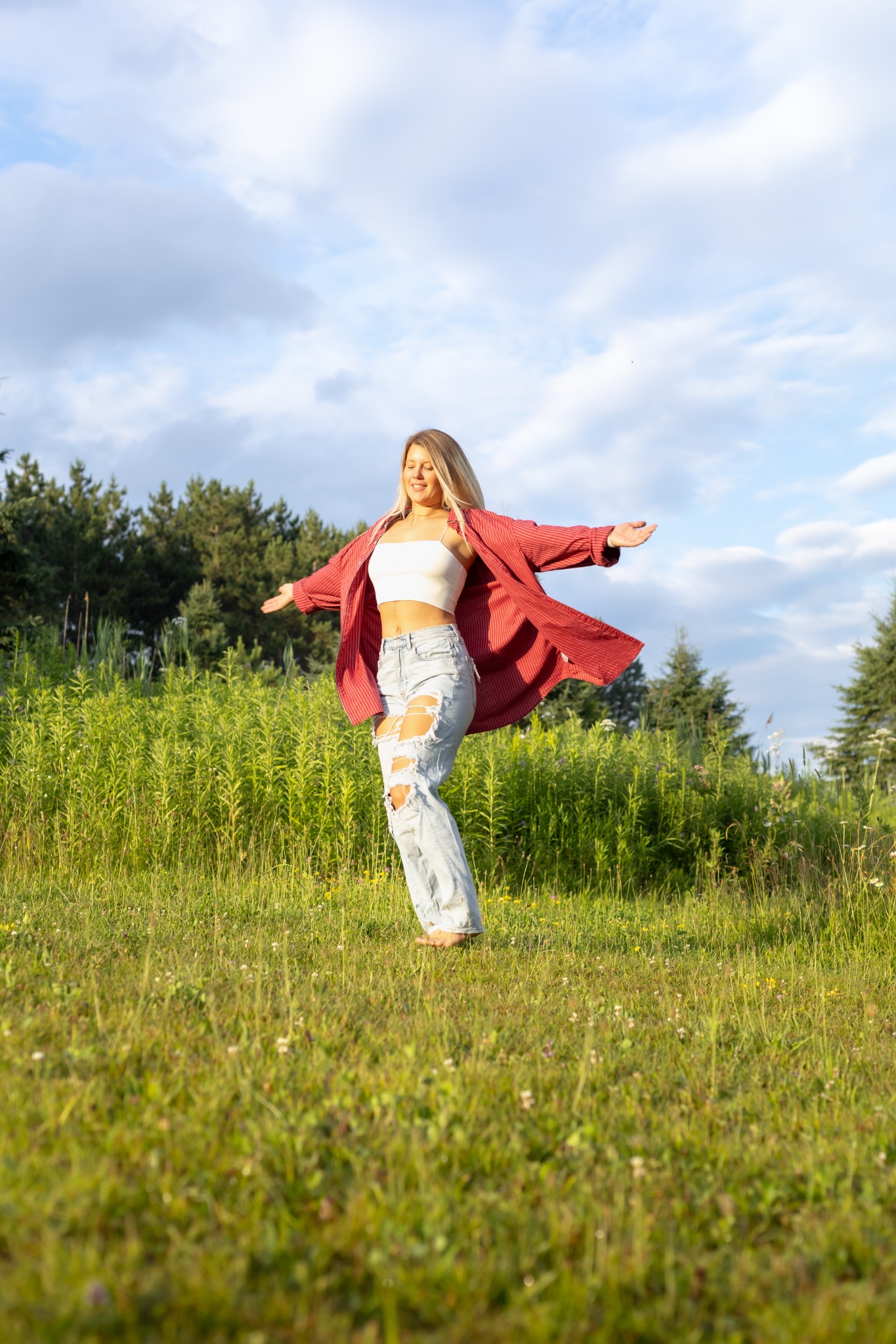 Mariane standing with her arms open in a sunlit meadow